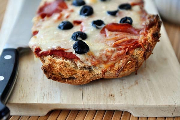 Baked pepperoni and olive french bread pizza on a cutting board.