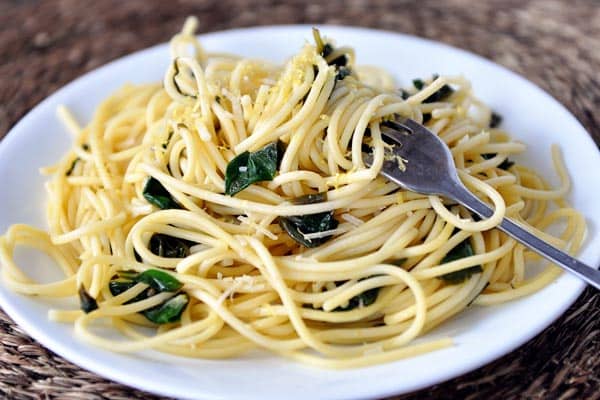White plate with cooked spaghetti with spinach sprinkled throughout.