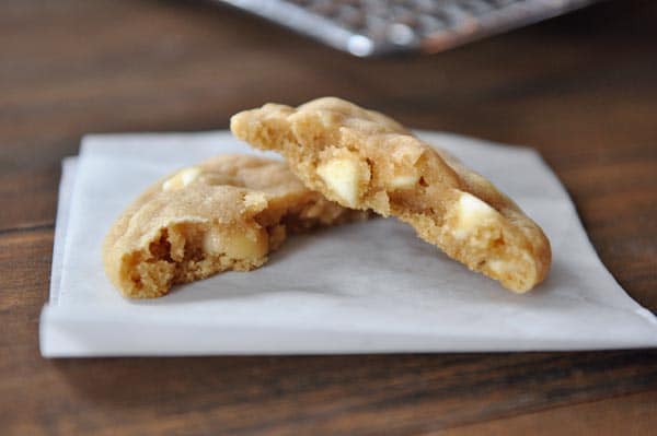A white chocolate macadamia nut cookie split in half on a piece of parchment paper.
