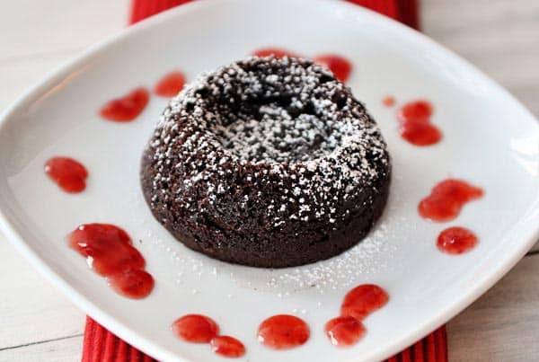 White plate with raspberry sauce and a chocolate molten cake sprinkled with powdered sugar.