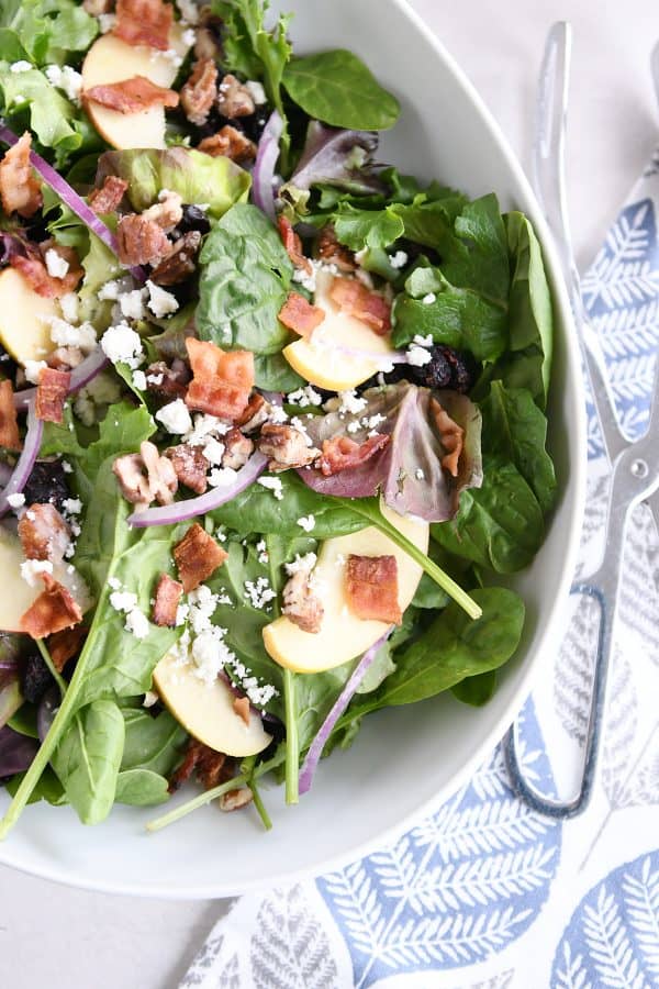 Top down view of spinach salad in white bowl.