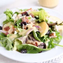 dished up portion of spinach salad on white plate with vinaigrette, bacon, onions and feta