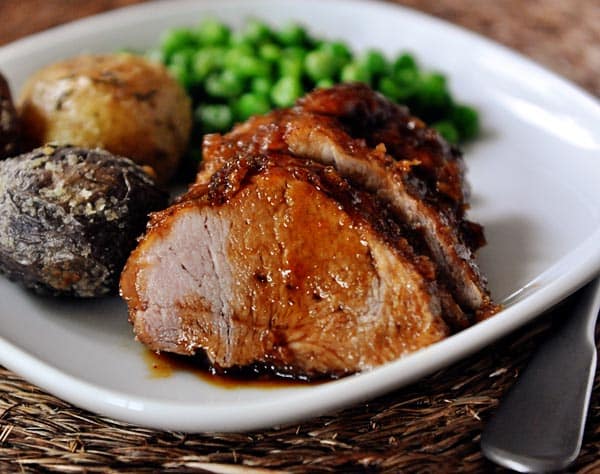 Roasted, sliced glazed pork tenderloin, with and red and purple potato and peas on the side. 