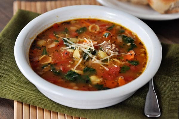 White bowl full of Tuscan sausage soup full of pasta shells and spinach and topped with Parmesan cheese.