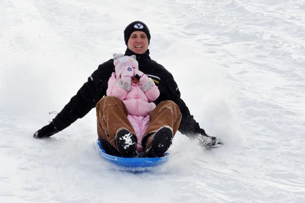 a man and little bowl sledding down a hill on a blue sled
