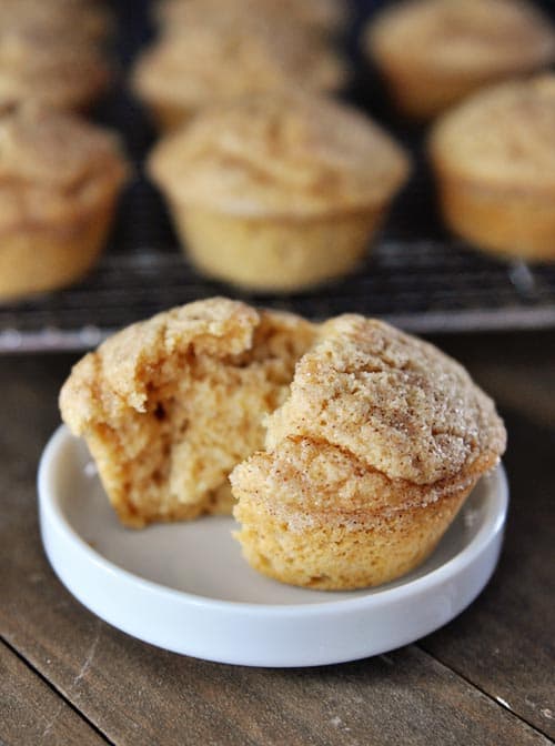 A split muffin on a white ramekin with other muffins on a cooling rack behind it.