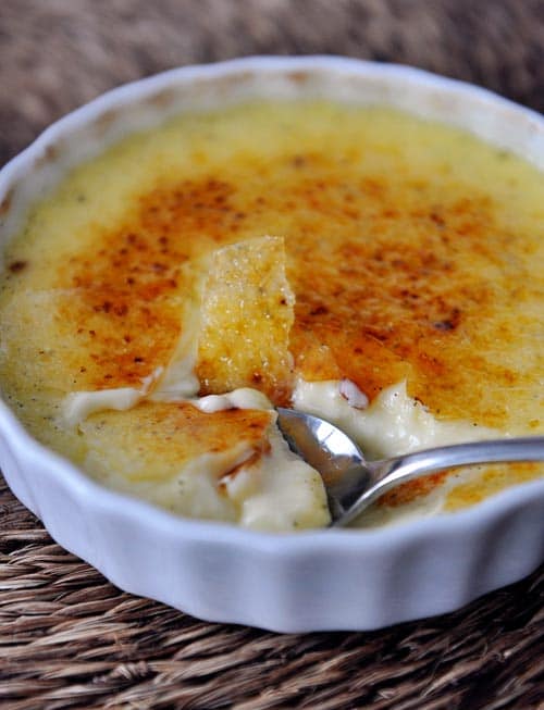 White ramekin full of creme brûlée with a spoon taking a bite out.