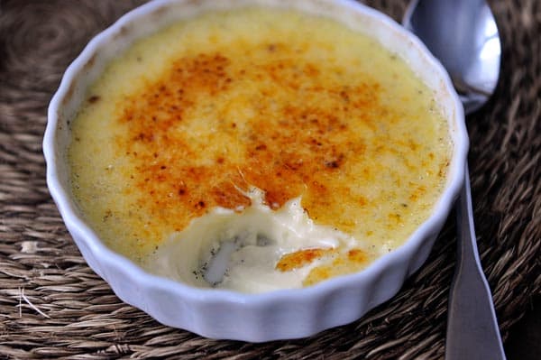 A white ramekin full of creme brûlée with a bite taken out.