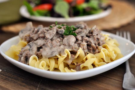 white plate with cooked noodles topped with ground beef stroganoff