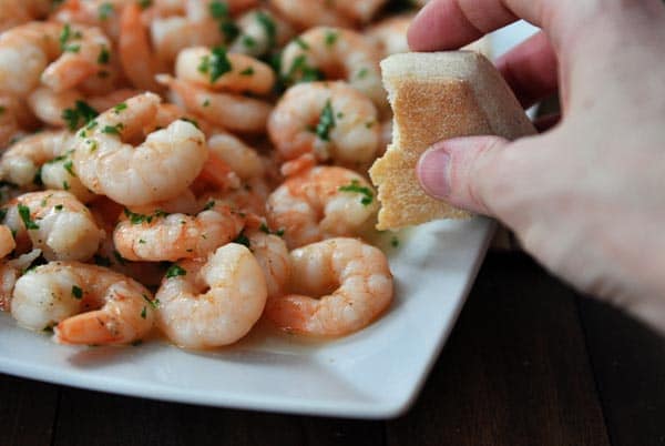 A platter of shrimp scampi with someone holding a half eaten roll over the top.