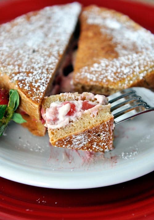 A strawberry cream stuffed french toast sprinkled with powdered sugar and a bite taken out.