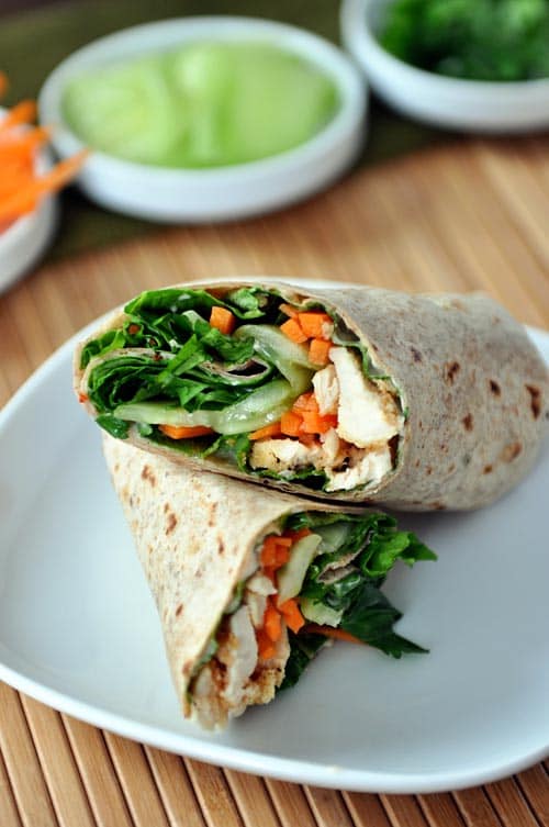 A chicken and vegetable-filled wrap split in half on a white plate.