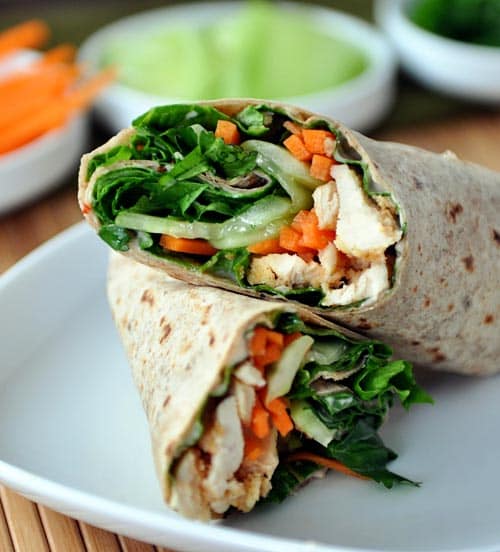 A chicken and vegetable wrap split in half on a white plate.