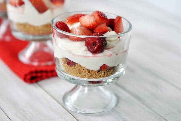 A layered no-bake berry cheesecake in a glass goblet topped with fresh berries.