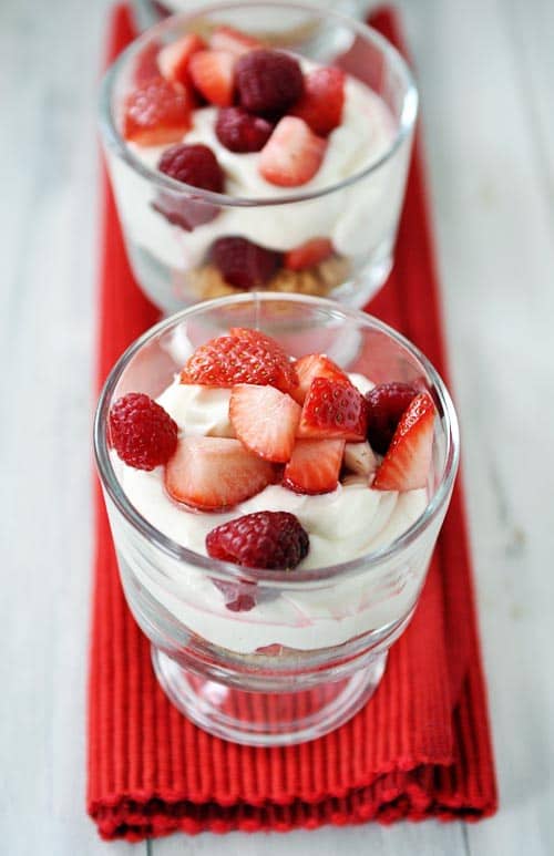 glass goblets full of berry yogurt cheesecakes topped with chopped strawberries