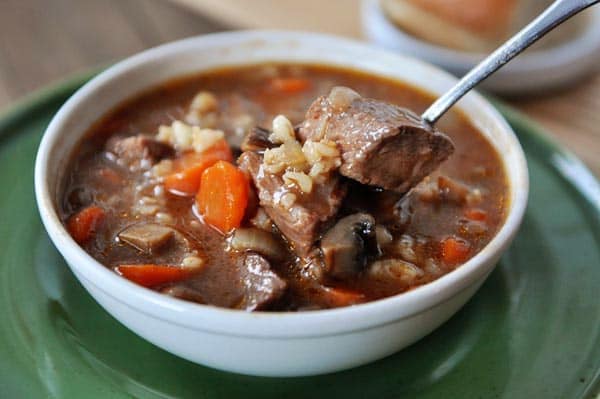 A white bowl full of a beef, veggie, and barley stew.