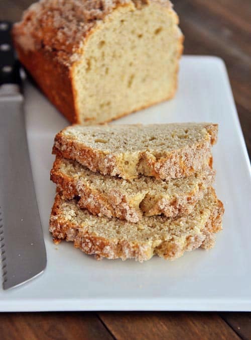 A loaf of streusel-topped banana bread with three slices cut out laying on a cutting board.