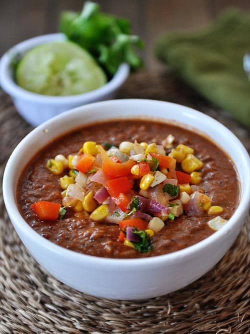 White bowl full of chili topped with tomato and corn salsa.