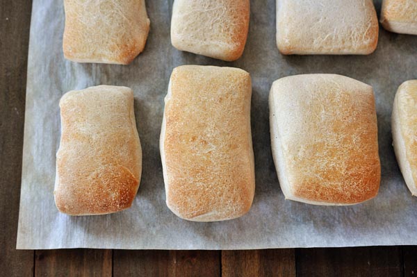 Top-down view of golden brown cooked italian rolls on a sheet of parchment paper.