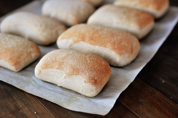 Light brown baked italian rolls lined up on a sheet of parchment paper.