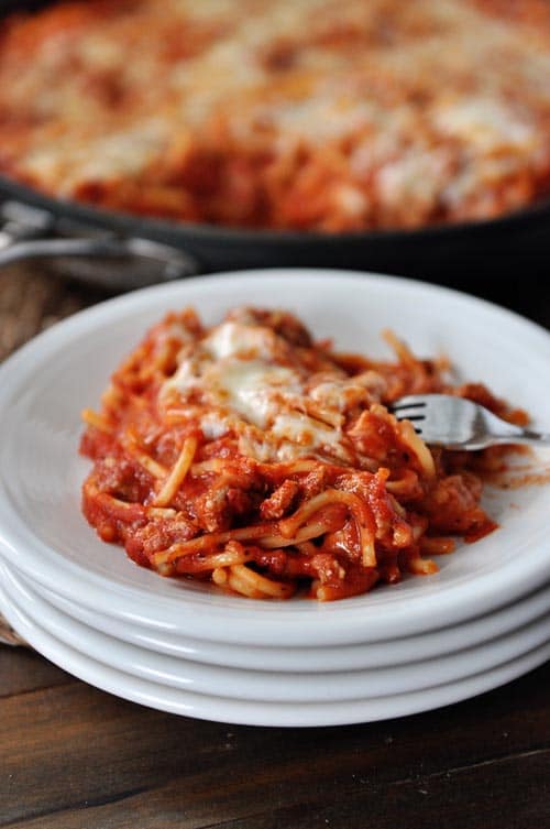 A stack of white plates with a helping of spaghetti on the top plate.