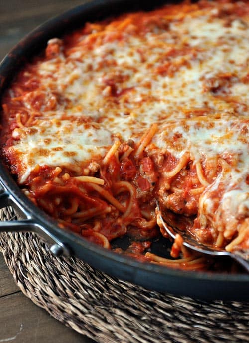 A cast iron skillet full of cheese-topped spaghetti.