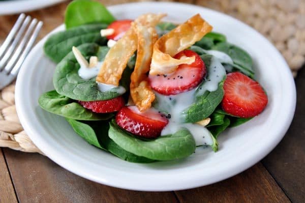 A spinach strawberry salad topped with croutons on a white plate.
