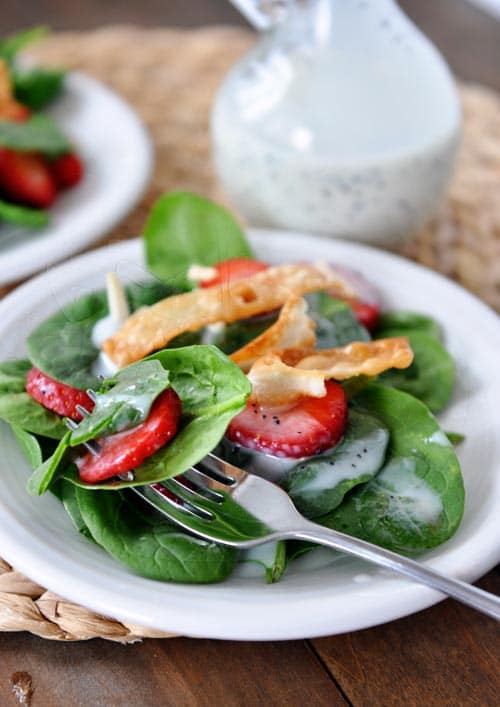 White plate full of spinach strawberry salad with a fork taking a bite out.
