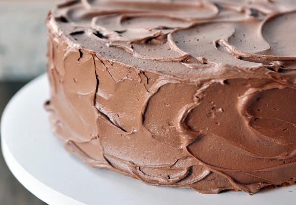 A cake covered in chocolate frosting on a white cake stand.