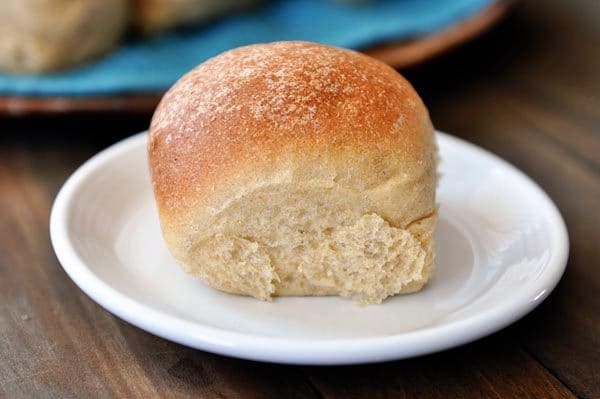 A golden brown whole wheat roll on a white plate.