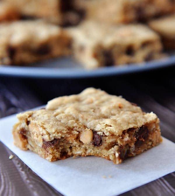 A chocolate chip peanut butter oatmeal bar with a bite taken out in front of a plate of other cut up bars.