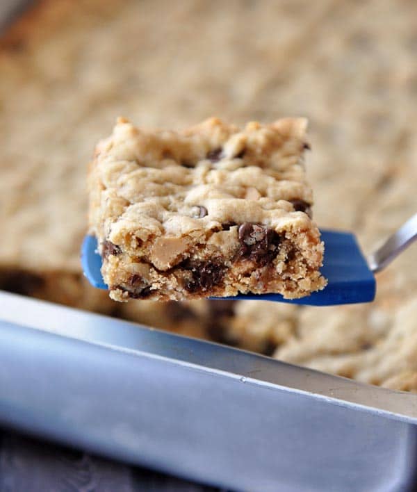 A small blue spatula holding a chocolate chip peanut butter oatmeal bar over a pan of the rest of the bars.