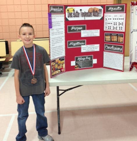 a little boy standing beside his science fair project