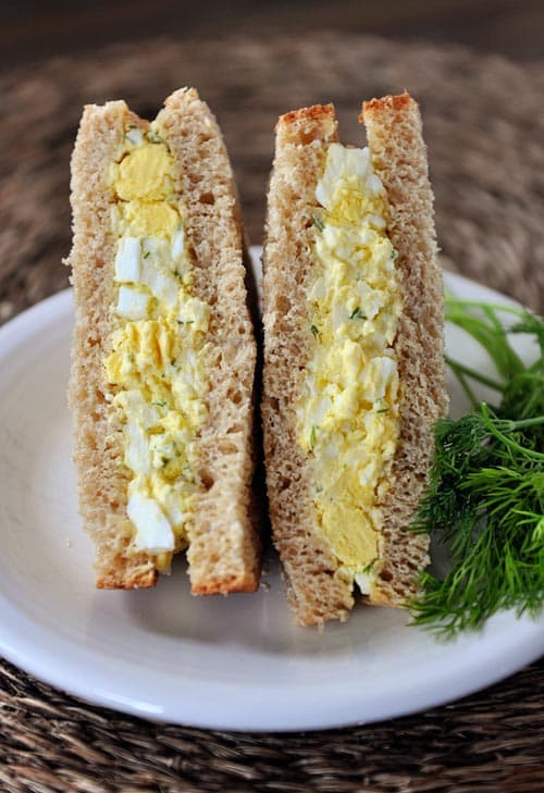 An egg salad sandwich cut in half on a white plate.