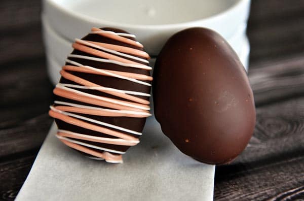 Two chocolate covered marshmallow eggs sitting against a stack of white plates.
