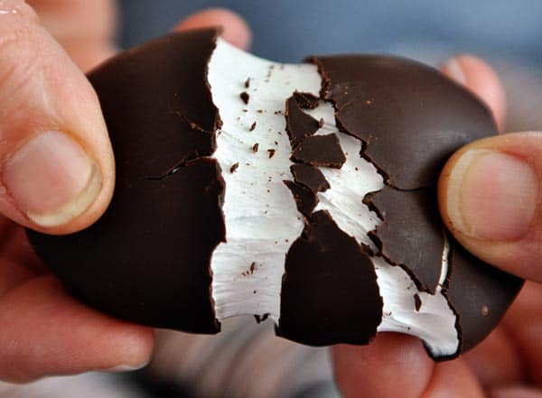 Hands pulling apart a chocolate marshmallow egg.
