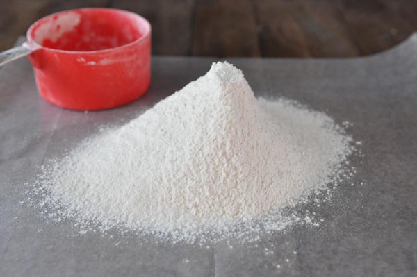 a mound of cake flour with a red measuring cup behind it