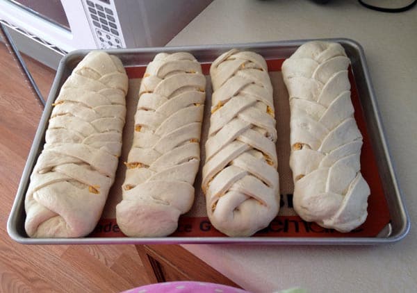 four uncooked braided breads on a cookie sheet