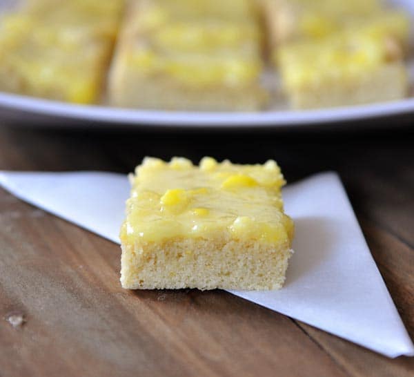 A lemon bar with lemon drops on top in front of a tray of more lemon drop bars.