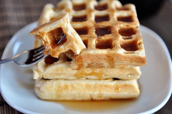 A stack of waffles covered in syrup on a white plate.