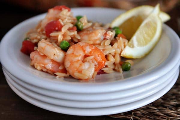 A stack of white plates with a helping of shrimp and orzo and two lemon slices on the side.