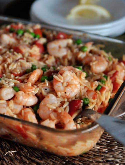 A glass baking dish full of shrimp, orzo, peas, and tomatoes.