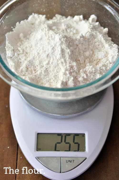 A glass bowl of flour on a scale being weighed. 