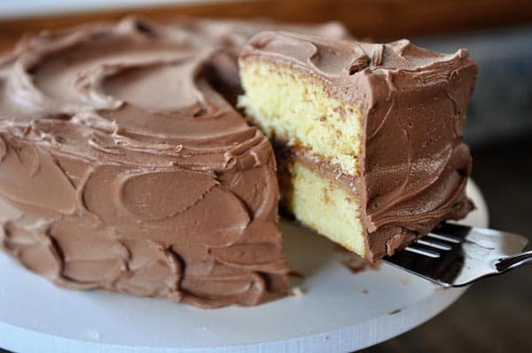 A cut slice of yellow cake with chocolate frosting being taken out of the take by a fork. 