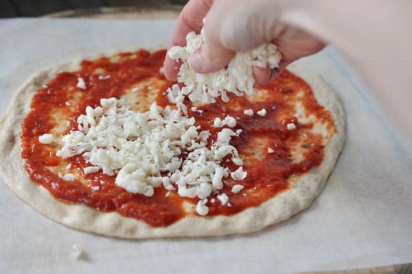 An uncooked pizza crust spread with red sauce getting cheese sprinkled on it. 
