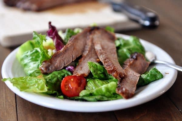 Sliced steak strips on top of a green salad on a white plate.