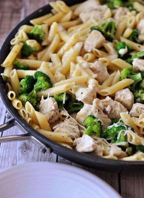 Top view of a skillet full of a chicken pasta broccoli meal sprinkled with parmesan cheese.