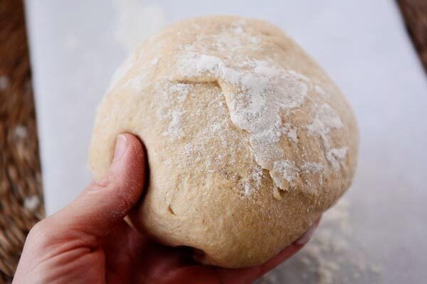 Hand holding a ball of uncooked whole wheat pizza dough. 