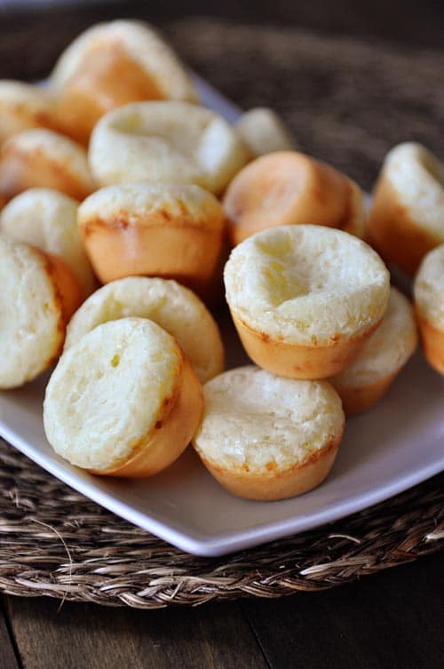 A white rectangular platter with a mountain of mini Brazilian pao de queijo breads.