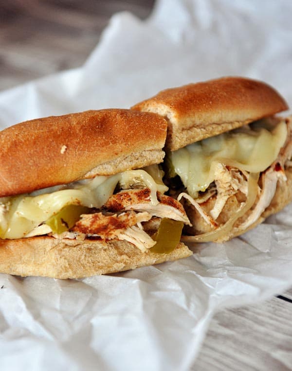 A Philly cheesesteak sub sandwich cut in half sitting on a piece of parchment paper.